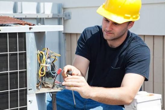 Technician checking electrical components inside an air-conditioning unit